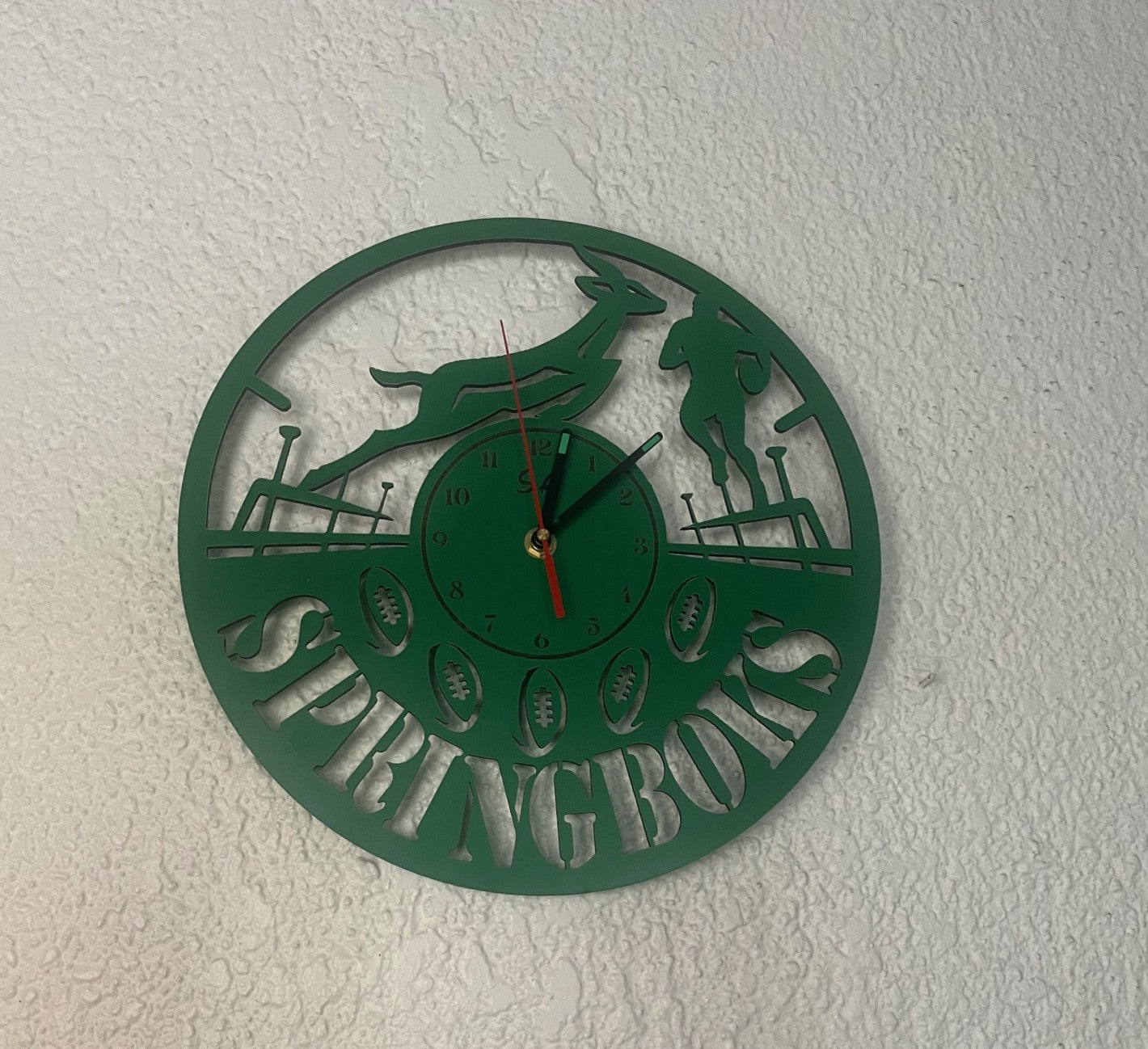Green wall clock with 'Springboks' design on a white wall